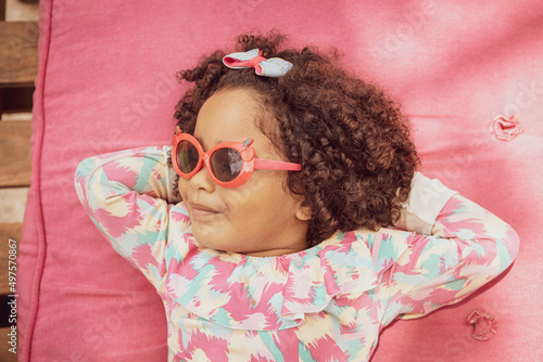 Portrait of smiling baby girl with afro hair style and sunglasses in a colourful swimsuit outfit. Afro-American and Afro-Brazilian children concept with copy space. photo