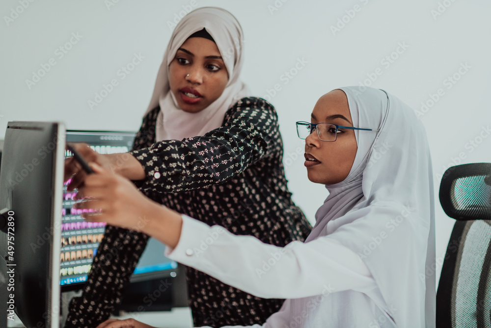 Friends at the office two young Afro American modern Muslim businesswomen wearing scarf in creative bright office workplace with a big screen Friends at the office two young Afro American modern Muslim businesswomen wearing scarf in creative bright office workplace with a big screen