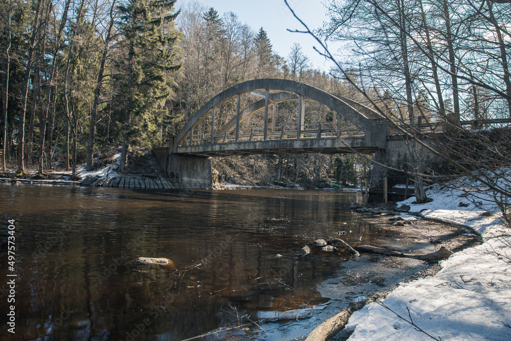 Old bridge across the river Spring landscape in April of a forest river. Snow lies on the shore. Finland. Old bridge across the river Spring landscape in April of a forest river. Snow lies on the shore. Finland.