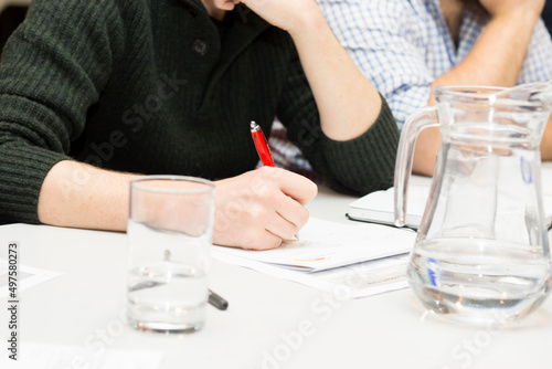 person writing on a not pad with a glass of water