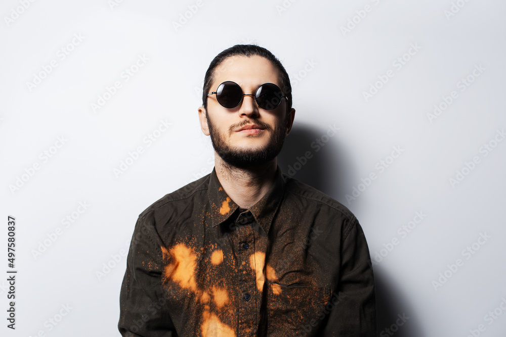 Fototapeta premium Portrait of young confident man wearing round sunglasses on white background.