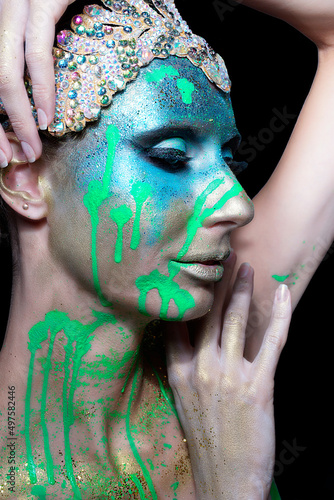 Sensual Woman in green paint and glitters . Woman on black background with Creative make up.Beautiful face with colored powder .