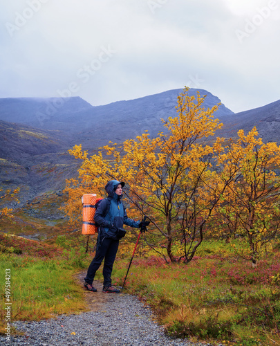 A woman with a backpack in the autumn season walks along a path in the mountains on a rainy day. © Andrey