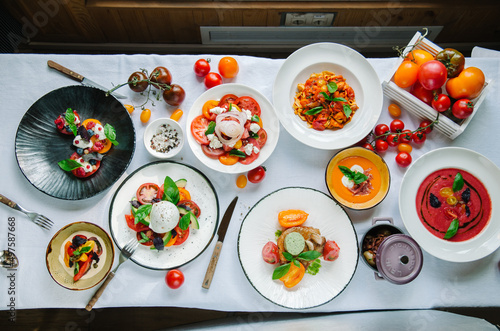 Variety of dishes on the table. Tomato menu in the restaurant, tomato soup, mix of tomatoes with buffalo mozzarella and pesto, pork fillet with baked. Restaurant menu. Italian cuisine. Top view