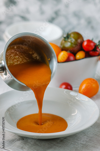 Delicious creamy tomato soup with herbs. Summer light yellow tomato soup. Soup is poured into a bowl
