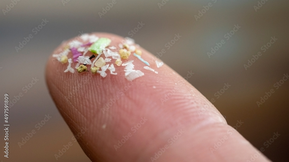 Close up side shot of microplastics on human fingers. Concept for water pollution and global warming.  Climate change idea. Soft focus on bunch of micro plastic that cannot be recycled.