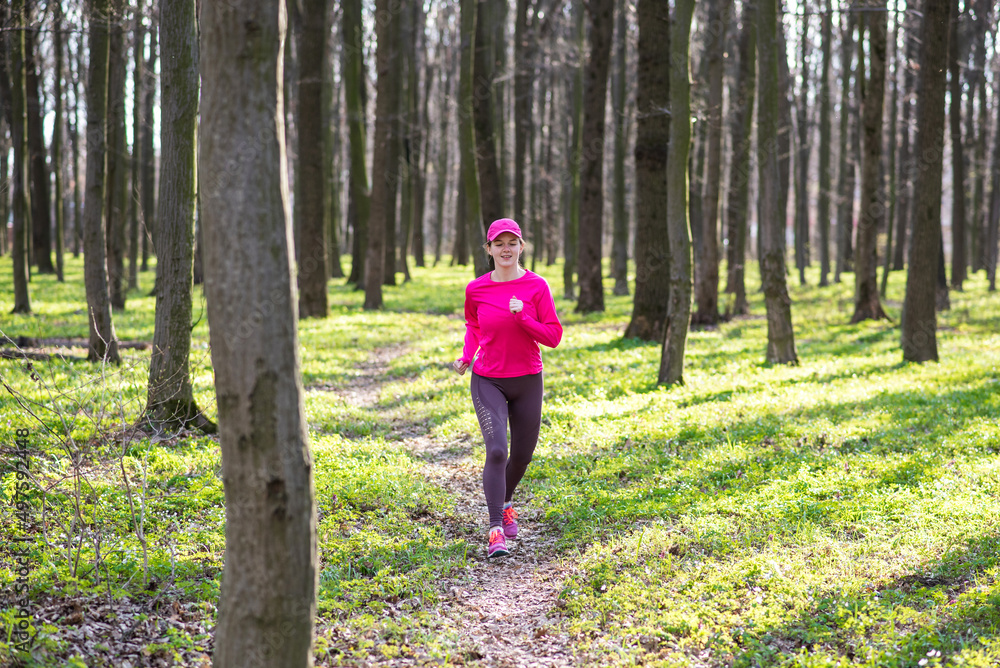 Sporty young female wearing rose clothes runs at a sunny spring forest along the pathway Sporty young female wearing rose clothes runs at a sunny spring forest along the pathway