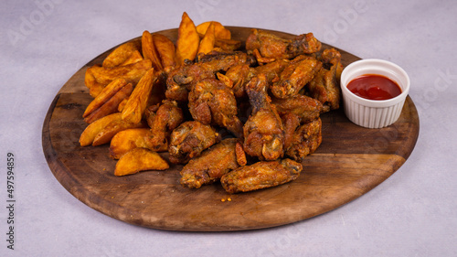 Closeup shot of fried chicken and potato fries with tomato sauce on a wooden round board photo