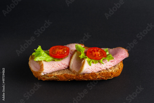 Sandwich of rye bread with ham, cherry tomatoes, lettuce on a black background.