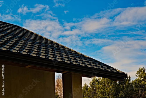Dach z blachy , imitującej dachówkę ceramiczną , na świeżo zbudowanym domu na tle błękitnego nieba z białymi chmurkami ( obłokami)  .