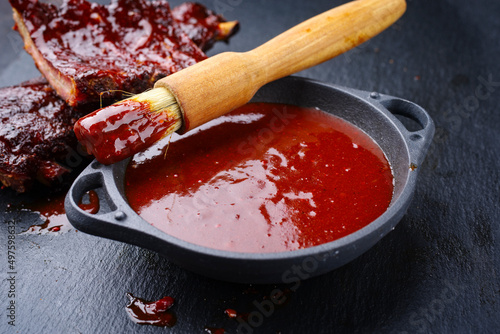 Hot and spicy barbecue sauce in a bowl as close-up with spare ribs in background photo