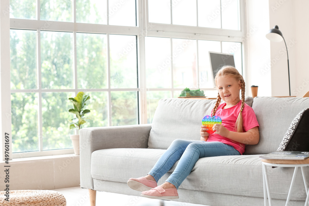 Girl sitting on sofa and holding pop it fidget toy in light room Girl sitting on sofa and holding pop it fidget toy in light room