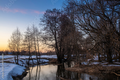 Dramatic sunset view over the river in winter; colorful sky and soft evening light; trees are reflected in the water