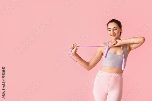 Sporty young woman with skipping rope on color background © Pixel-Shot