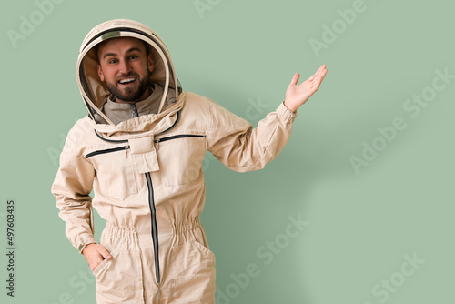 Male beekeeper in protective suit showing something on green background
