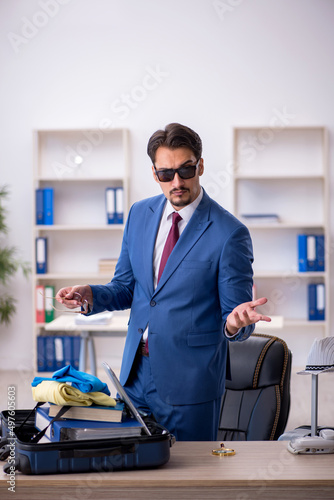 Young male employee preparing for trip at workplace