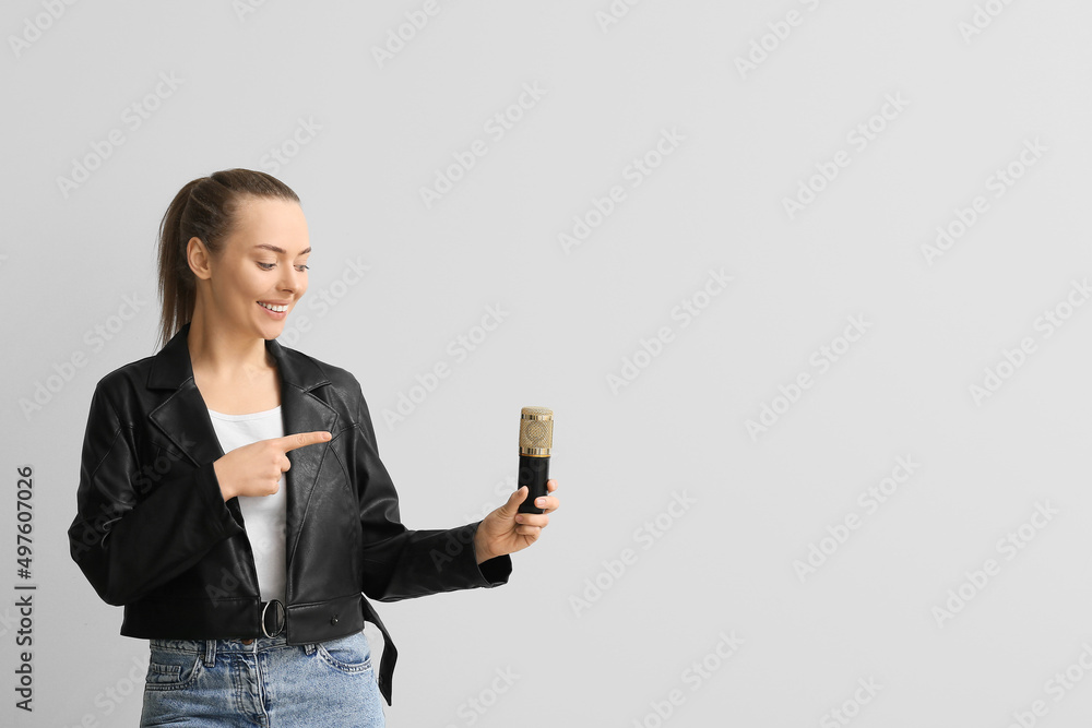Young woman pointing at professional microphone on light background Young woman pointing at professional microphone on light background