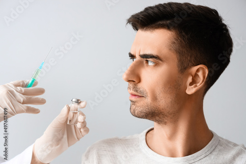 Handsome man with hair loss problem receiving injection on light background