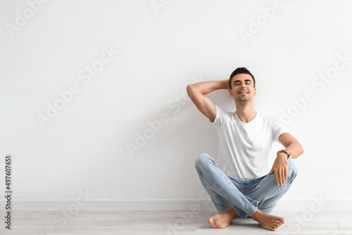 Young barefooted man sitting near light wall