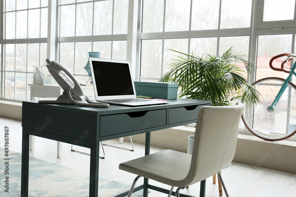 Workplace with modern laptop and landline phone in light office Workplace with modern laptop and landline phone in light office