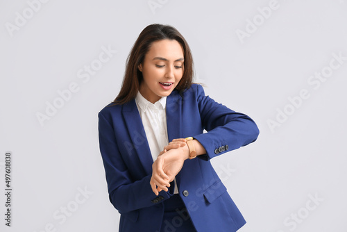 Fotografering Portrait of young secretary looking at watch on light background