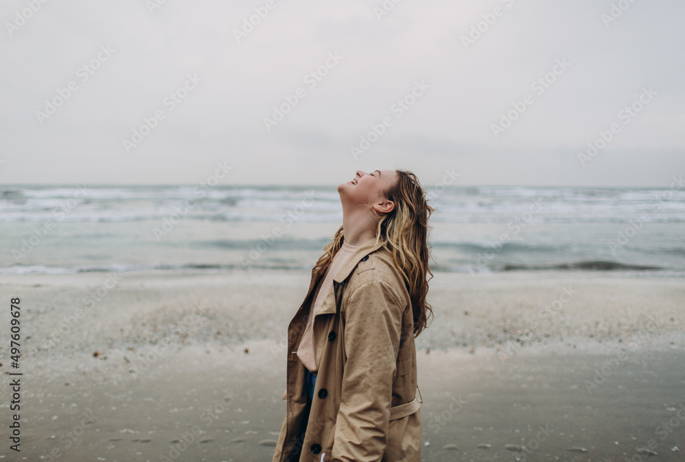 in the photo, a young beautiful blonde curly girl smiles and has fun outdoors against the backdrop of a foggy sun through thick fog on a calm sea and blue sky in the photo, a young beautiful blonde curly girl smiles and has fun outdoors against the backdrop of a foggy sun through thick fog on a calm sea and blue sky