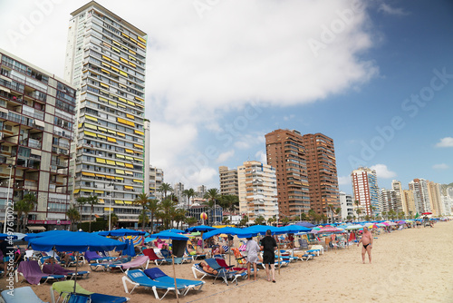 2021.08.18 Benidorm, Spain Beach near living buildings with sunbathing beds. People enjoy under a sunshade. High-quality photo