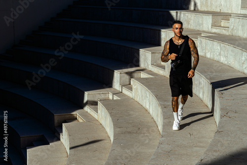 Caucasian sporty male with tattoos standing in the stone stair architecture