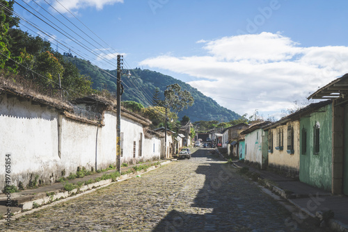 Town of Ataco in Ruta de las Flores, El Salvador. Empty road with sidewalk and old buildings. View of tree covered hills in the distance