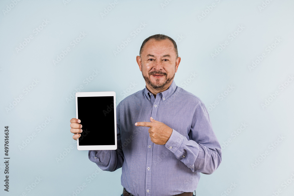portrait of hispanic senior man wearing casual clothes and holding a tablet on blue background in Mexico Latin America portrait of hispanic senior man wearing casual clothes and holding a tablet on blue background in Mexico Latin America
