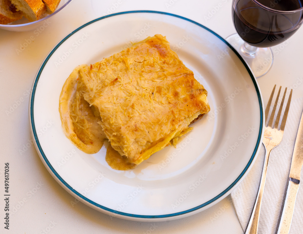 Slice of lasagna with melted cheese on top and minced meat filling on a plate in a restaurant