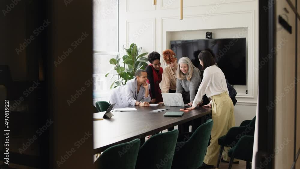 Slow motion view through open doorway towards group of businesswomen discussing with laptop on meeting room table Slow motion view through open doorway towards group of businesswomen discussing with laptop on meeting room table