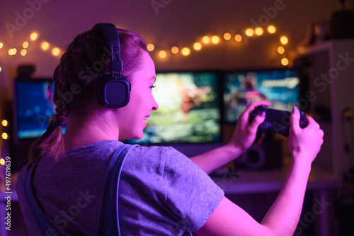 Gaming and e-sports. A streamer girl plays games using the joystick and gamepad. On three monitors, creative light © Anton