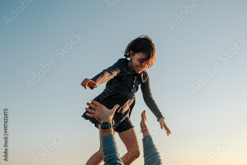 Young girl high above father's arms