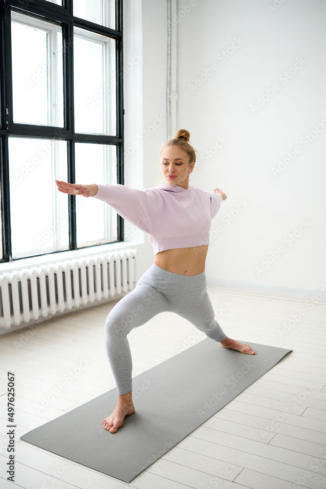 Woman training yoga in Virabhadrasana near window Woman training yoga in Virabhadrasana near window
