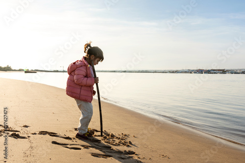 Little girl drawing with stick on the seashore photo