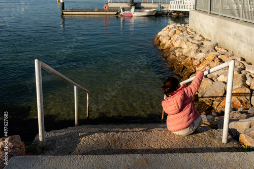 Girl sitting looking at boats on jetty photo