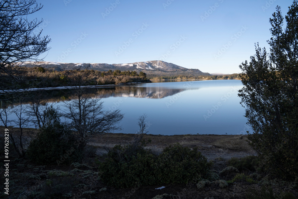 View of the peaceful lake in a summer sunny day. The forest, mountains and blue sky reflection in the water surface.