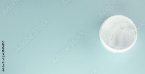 White cosmetic face cream in a round open jar on a light blue background, top view, copy of the space on the left