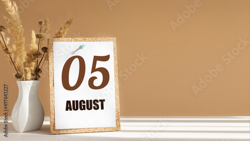 august 5. 5th day of month, calendar date.White vase with dead wood next to cork board with numbers. White-beige background with striped shadow. Concept of day of year, time planner, summer month photo