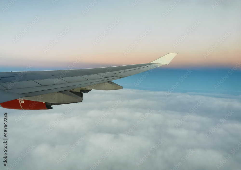 Fototapeta premium View from the porthole on the wing of an airplane with a red aircraft engine flying above beautiful white clouds.