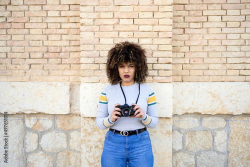 Serious woman with photo camera near brick wall photo