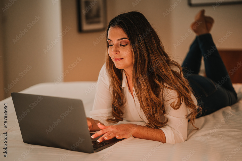 Woman typing on keyboard of laptop on bed Woman typing on keyboard of laptop on bed