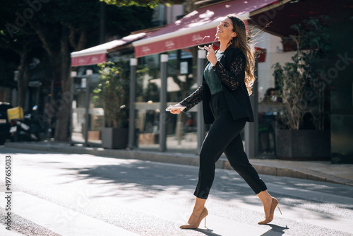 Smiling woman in formal wear crossing road on crosswalk