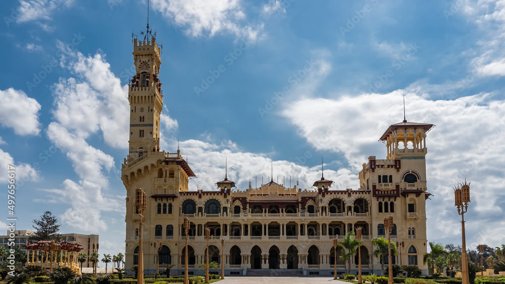 The old Montazah Royal Palace in the park of Alexandria. Arched openings and colonnades are visible. Tall towers against a background of blue sky and clouds. Egypt.