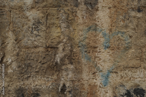 Faded graffiti of a blue heart on an ochre stone wall