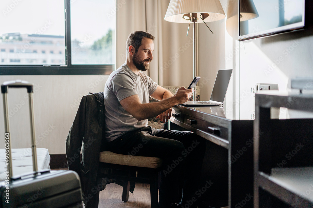 Adult man browsing smartphone and working on laptop Adult man browsing smartphone and working on laptop