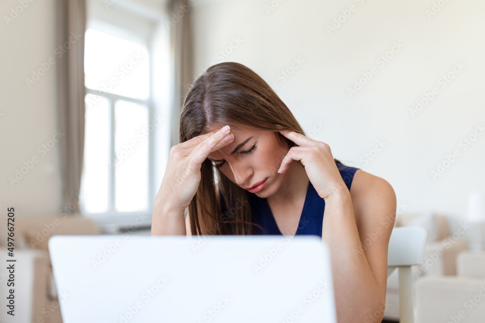 Young frustrated woman working at office desk in front of laptop suffering from chronic daily headaches, treatment online, appointing to a medical consultation, electromagnetic radiation, sick pay Young frustrated woman working at office desk in front of laptop suffering from chronic daily headaches, treatment online, appointing to a medical consultation, electromagnetic radiation, sick pay