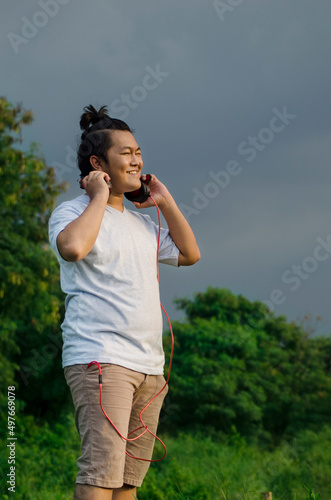 asian male model handsome smile wearing t-shirt and casual short listening to music song using headphone while squinting his eyes from the glare of the light
