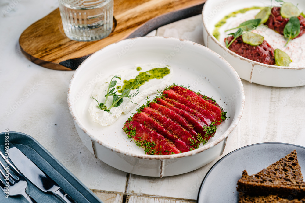 Gravlax, Scandinavian dried salmon with feta mousse on a white plate and Veal tartar with truffle sauce and pickled cucumber Gravlax, Scandinavian dried salmon with feta mousse on a white plate and Veal tartar with truffle sauce and pickled cucumber